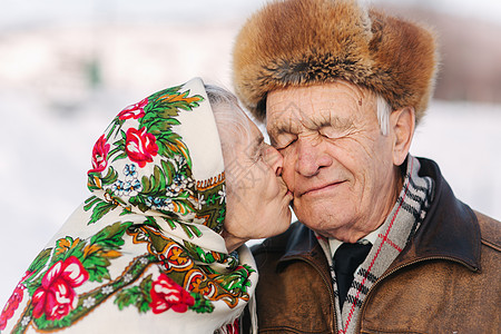 愉快的年长夫妇画象 老妇人重重地亲吻她的丈夫 老夫妇在冬天的时候在公园散步 幸福的家庭 金婚婚礼季节疾病乐趣老年人皱纹男人退休微图片