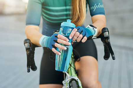专业女骑自行车的女性持水瓶 休息 白天站着脚踏车到户外露天休息的裁剪镜头图片
