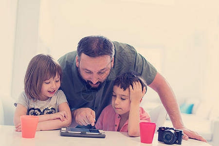 在家的单身父亲 有两个孩子在平板电脑上玩游戏幸福微笑父母孩子们技术男性童年互联网男人女性图片