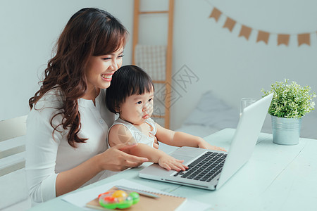 工作母亲概念 在家与孩子一起使用笔记本电脑的年轻妇女电话女儿人士女士互联网婴儿女孩讲话男生父母图片