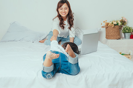 亚裔年轻女性在笔记本电脑上忙碌 而她女儿却在母亲身边玩耍女孩母性技术婴儿幸福互联网父母家庭工作孩子图片