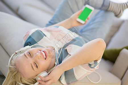 女孩通过耳机享受音乐幸福快乐休息喜悦房子生活技术房间沙发微笑图片