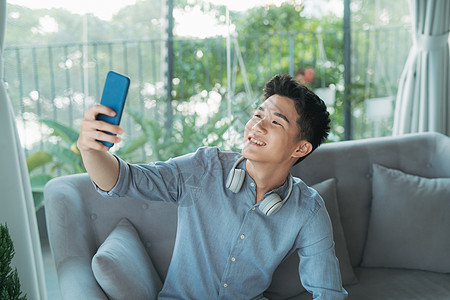 英俊的年轻帅哥穿着无线耳机自拍听音乐手机技术男人幸福微笑快乐男性乐趣电话工具背景图片
