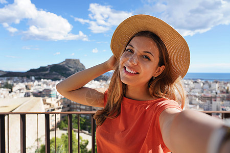 圣费尔南多城堡的旅游女孩与阿利坎特城市景观和贝纳坎蒂尔山的自拍合影 背景是圣巴巴拉城堡 女孩在西班牙阿利坎特自拍图片