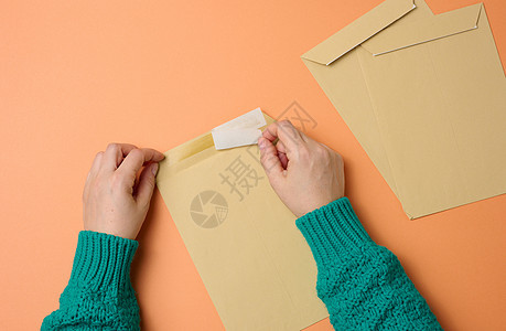 女性手持纸袋 放在橙色背景的顶端视图上邀请函问候语卡片白色文档棕色商业成人手指邮件图片