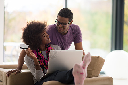 非裔美裔情侣在网上购物幸福闲暇互联网沙发卡片笔记本男性成人房间微笑图片