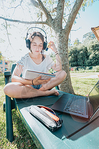 坐在花园里微笑着为大学学习的年轻女子喜欢户外休闲听音乐和使用笔记本电脑 房子研究 人们的生活方式概念图片