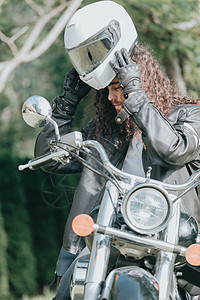 一个年轻的长发男子的肖像 一个穿着皮夹克的老骑自行车的人 骑着复古自行车 老式经典摩托车 自由和风格的概念 一种对生活的爱好 复图片