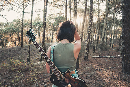 一名年轻女子在日落时拿着吉他后背拍摄 享受音乐生活的概念图片