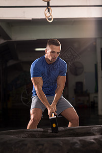 使用铁锤和拖拉机轮胎进行人手锻炼耐力专注男人健美运动成人活力健身房二头肌运动员图片