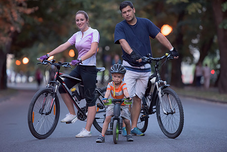 有自行车的年轻家庭男性微笑公园闲暇骑术女性男人头盔行动儿子图片