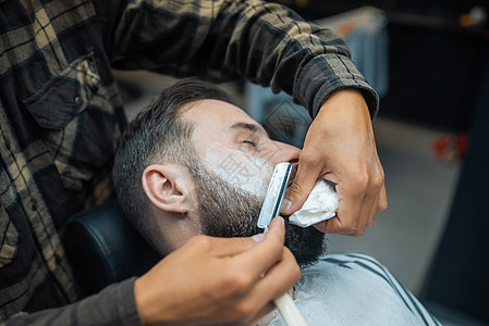 在理发店被理发师理发师剃胡子的年轻胡须男剃刀工作男性客户治疗理发服务潮人成人头发图片