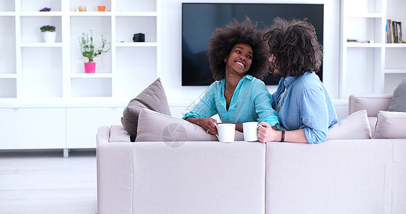坐在沙发上在家喝咖啡的多民族夫妇男朋友男性微笑妻子女孩丈夫家庭男人幸福房间图片