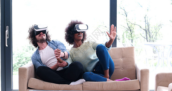 使用虚拟现实耳机的多种族夫妇耳机创新乐趣房间娱乐活动技术男人沙发女士图片