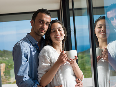 在家放松的年轻夫妇长椅杯子亲热窗户财产女性丈夫房子女士拥抱图片