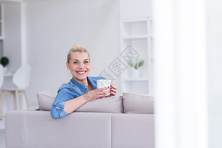 女人喜欢喝一杯咖啡微笑女孩沙发公寓香气长椅杯子女士乐趣女性图片