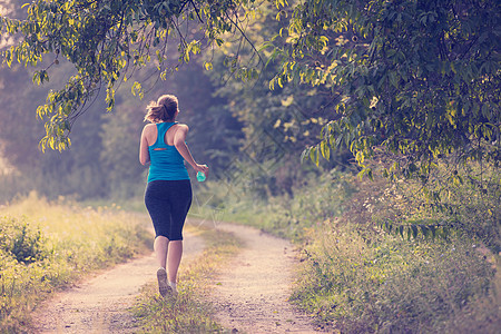 妇女在乡村公路上慢跑冒险森林运动员自由衣服阳光国家锻炼跑步女孩图片