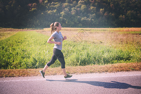 妇女在乡村公路上慢跑锻炼慢跑者活力阳光衣服女士训练赛跑者森林运动装图片