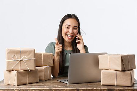 小企业主 创业和电子商务概念 微笑的亚洲女商务人士 网店经理指着相机 接听客户电话 用笔记本电脑接单 装运包装箱企业家人士广告售图片
