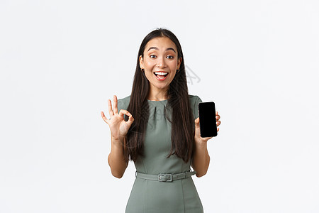 小企业主 女企业家的概念 满意的亚洲女性客户 穿裙子的女性展示智能手机屏幕应用 做出好的手势 推荐应用代理人传递技术办公室商业博图片