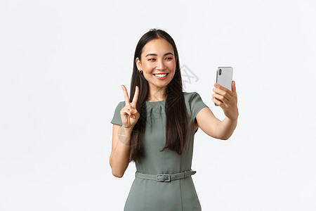 小企业主 女企业家的概念 漂亮的亚洲女性博主在智能手机上自拍 摆姿势 看着带有和平标志的手机摄像头雇主裙子代理人女孩保险消息工作图片