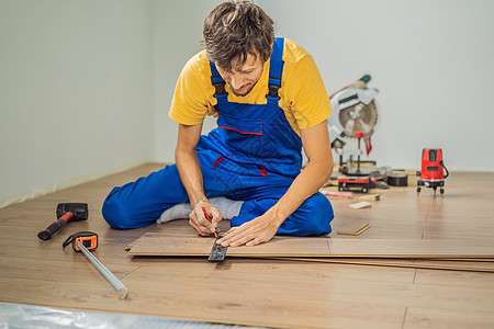 男人在温暖的薄膜地板上安装新的强化木地板 复合地板下的红外线地暖系统教学男朋友微笑铅笔职业工具箱瓦工锤子地面维修图片