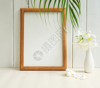 将海报木板和美丽的弗朗吉帕尼热带花朵装上现代白花瓶 放在蜜蜂桌上 并用绿棕榈叶在木壁背景上图片
