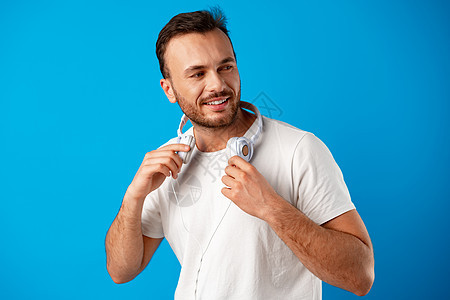 穿轻便白色T恤衫的青年男子 蓝底带耳机图片