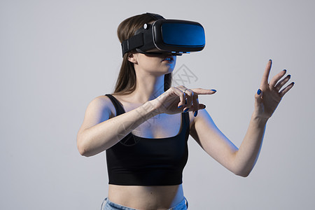 身着VR眼镜的年轻女性站在摄影棚里 在虚拟空间亲手擦拭滚动放大镜 同时在社交网络上与物体互动 笑声虚拟现实桌子互联网技术团队手势图片