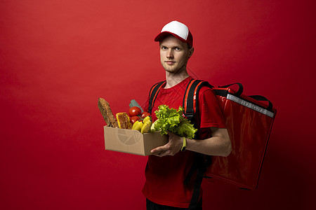 带热袋的红制服男雇员携带纸盒包 红色背景有杂货 产品从商店或餐馆运到家里 复制空间 请查看InfoFinland上的图片