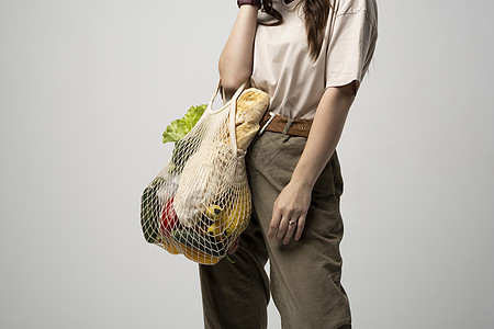 微笑的年轻女子的画像 穿着超大号 T 恤 拿着可重复使用的网袋和杂货 用于购物的可重复使用的生态袋 零废物 无塑料概念 生态生活图片