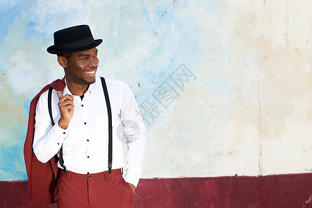 冷酷的非洲男性时装模特 笑着穿着旧西装 吊带和墙上帽子图片