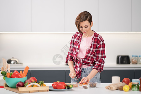 在家为有爱的家人做饭 漂亮的年轻女人站在厨房里 在桌上切食材 做午餐或晚餐 健康的食物生活 健康的生活方式图片