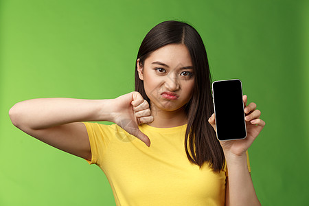 特写失望心烦意乱的亚洲女孩判断糟糕的糟糕应用程序 显示智能手机屏幕 拇指向下的鬼脸不高兴 给出负面反馈 无法忍受前男友的新女友互图片