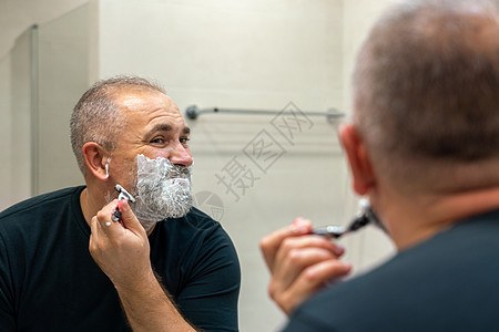 中年帅哥修剪胡须站在浴室里照镜子泡沫镜子奶油凝胶剃刀胡子刮胡子隔断白发头发图片