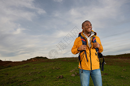 快乐的年轻黑人男子在田地上背着背包的肖像成人娱乐天空生活风衣男人远足自由男性运动图片