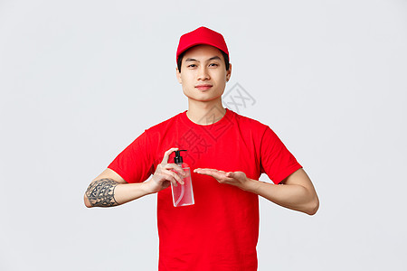 隔离 安全无接触的交付和在线购物概念 以红色帽子和T恤衫微笑着像亚洲人一样送货的人手上施用洗手剂 以防止食肉19和病毒传播互联网图片