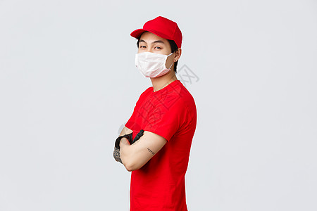 自信的亚洲送货员戴着红帽 医用口罩和手套 双臂交叉胸前站立 以自信的表情转向镜头 确保安全快速的承运人工作 快递概念运输邮递员员图片
