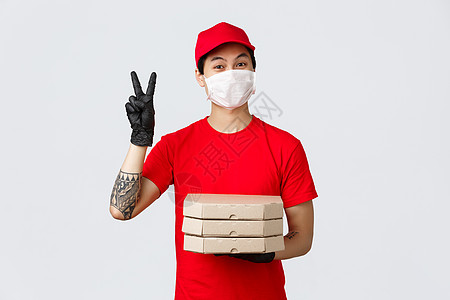 身戴医疗面具和手套 戴着红色制服帽子 持有披萨盒并制作和平标志见客户 提出在病毒爆发期间无接触运送食物的建议 共食19次商业命令图片