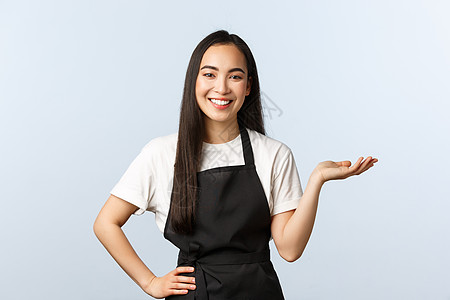 咖啡店 小型企业和创业概念 开朗友善的女服务员 身穿黑色围裙的亚洲女咖啡师在咖啡馆菜单中介绍新产品 甜点或饮料 向右指图片