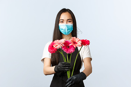 小型企业 冠状病毒流行病 订单和商店概念 微笑迷人的女花店 店主或员工戴着医用面具和防护手套 给顾客购买的花束图片