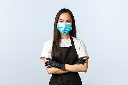 Covid-19 流行病 社会距离 小企业和预防病毒的概念 自信可爱的亚洲咖啡师 咖啡店员工保护顾客 使用医用口罩和手套 交叉双图片