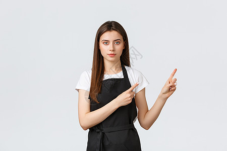 小型企业 员工和咖啡店的概念 年轻坚定的女咖啡馆员工指着广告的右上角 穿黑围裙的可爱女售货员提供信息图片