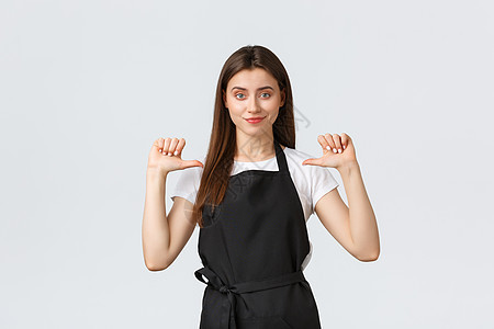 小型企业 员工和咖啡店的概念 穿着黑色围裙 自信 帅气的女咖啡师指着自己 高兴地笑着 炫耀 成为本月最佳员工图片
