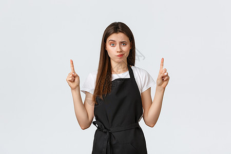 小型企业 员工和咖啡店的概念 怀疑和失望的女咖啡师不满意地笑着 用手指指着奇怪的广告 白色背景图片
