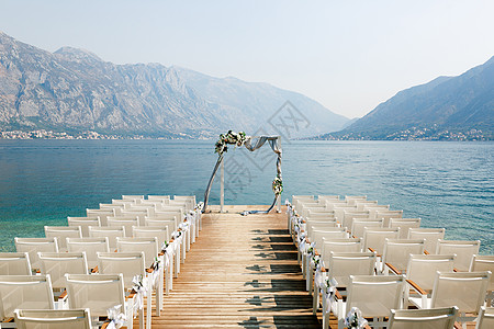 婚礼山湖婚礼拱门站在一排椅子的前面 就在一个木头码头上 俯视着山峰背景
