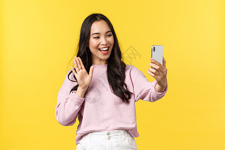 人们的情绪 生活方式 休闲和美貌概念 可爱的离任亚洲女孩与朋友通过视频电话交谈 手挥手在电话相机上打招呼 博客有实况流 黄色背景图片