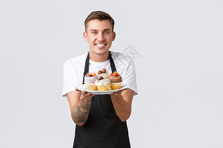 小型零售企业 咖啡店和面包店的概念 友好英俊的咖啡师展示新菜单 盘子里美味的纸杯蛋糕 侍者点菜 白色背景中的美味松饼图片