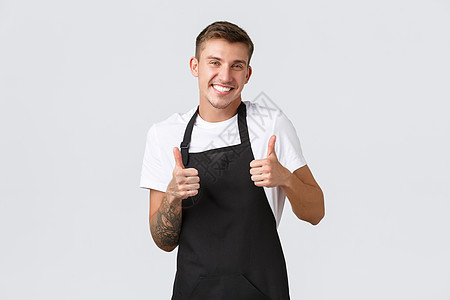 员工 杂货店和咖啡店的概念 咖啡馆帅气友善的男工 店员穿着黑色围裙 竖起大拇指 微笑欢迎客人 保证质量图片