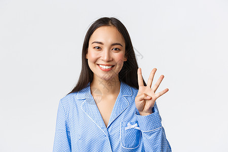 身穿蓝色睡衣的快乐迷人亚洲女性特写镜头 展示四根手指和微笑的白牙 解释主要规则或下达命令 站在白色背景上很高兴图片